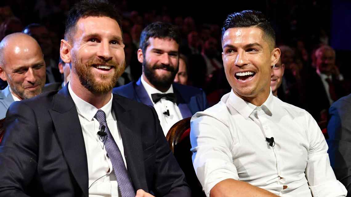 Messi e Cristiano Ronaldo sentados lado a lado e sorrindo durante sorteio dos grupos da Champions League temporada 2019/2020